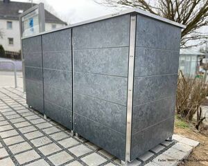 Ein grauer Metallschrank im Freien auf Pflastersteinen.