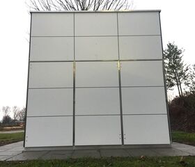 Ein modernes, weißes Gebäude mit quadratischen Paneelen, steht auf gepflastertem Boden, umgeben von Bäumen und Gras.