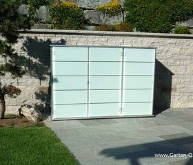 . Ein Gartenregal aus Glas und Metall steht an einer Steinmauer, umgeben von Pflanzen und Rasen.