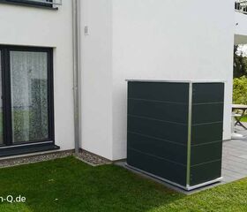 . Außenbereich eines Hauses mit Terrassentisch, Pflanzenkübel und einem modernen, dunkelgrauen Gartenschrank.