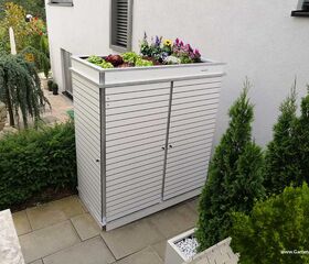 . Ein Gartenschrank mit bepflanztem Dach in einem modernen Garten mit Pflanzen und Statuen.