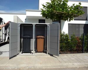 . Ein Mülltonnenunterstand mit zwei geöffneten Türen, darin schwarze und braune Mülltonnen.