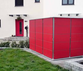 . Ein rotes Gartenhaus steht vor einem weißen Gebäude mit einer roten Tür und Garten.