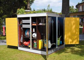 . Ein geöffneter Gartenschrank enthält Gartengeräte, Spielzeug, einen Ball, Schläuche und andere Gartenartikel.