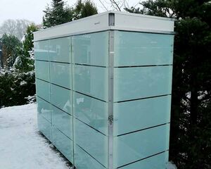 Es ist ein moderner Gartencontainer oder Geräteschuppen mit Glasoptik, umgeben von schneebedeckten Bäumen.