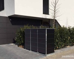 Ein modernes Gebäude mit dunkelverkleideten Paneelen, Pflanzen und einer schwarzen Mülltonnenbox im Vordergrund.