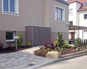 . Moderne Hausfassade mit großem Fenster, kleine Gartenanlage und Steinweg davor.