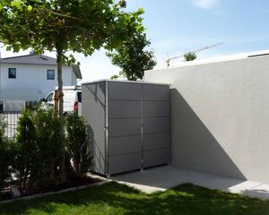 . Moderner Garten mit Metallbox, Baum und Sträuchern; Haus und Kran im Hintergrund.