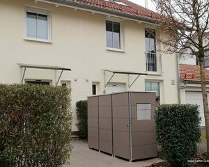 Ein modernes Wohnhaus mit roten Ziegeln, Strauchhecke und grauem Gartenhaus im Vorgarten.