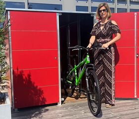 . Eine Frau zieht ein grünes Fahrrad aus einem roten Schuppen im Freien.