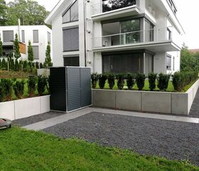 . Moderne zweigeschossige Häuser, gepflegter Garten, Sträucher, graue Steinwege, Rasenmäher auf Gras.