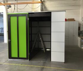 Ein grüner Türrahmen in einer Werkstatt öffnet sich zu einem kleinen Raum mit einer Leiter darin.