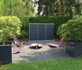 . Ein Garten mit zwei Liegestühlen, einen Feuerstelle, zwei große Pflanzen in Behältern und einem Tier auf Kies.