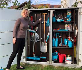 Eine Frau steht neben einem geöffneten Gartenschrank mit verschiedenen Gartengeräten und Werkzeugen.