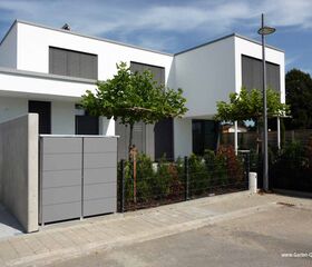 Modernes Doppelhaus mit weißen Fassaden, großen Fenstern und kleinen Bäumen im Garten.