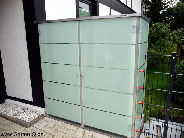 . Ein modernes Gartenlager mit satiniertem Glas, neben einem Zaun und Kiesbeet, mit Website-Name unten links.