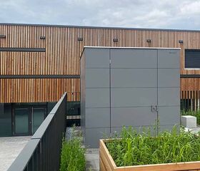 Ein modernes Gebäude mit Holzverkleidung, grauer Struktur und Hochbeet mit Pflanzen.