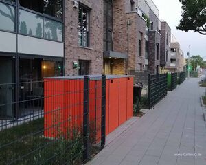 Appartementhaus mit Backsteinfassade, rotem Zaun, Gehweg und Baum.