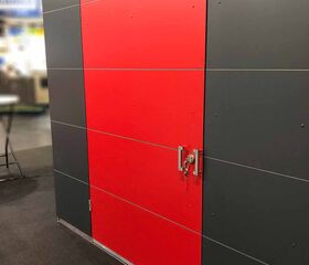 Ein grauer Schrank mit einer roten Tür und einem Schloss, ausgestellt auf einer Messe.