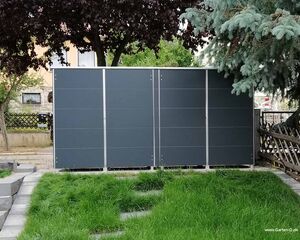 . Ein modernes Gartenhaus mit dunklen Paneelen, umgeben von Bäumen und Rasen.