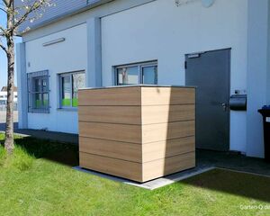 Ein großer, rechteckiger Holzcontainer steht neben einem Gebäude mit einer Tür und einem Fenster.