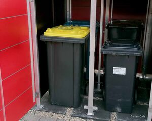 Mülltonnen mit Farbdeckeln in einem Abstellraum mit roter Tür.