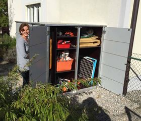 . Eine Frau steht vor einem geöffneten Gartenschrank mit Werkzeugen und Zubehör.