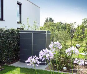 Ein moderner Gartenschuppen neben einem Haus, umgeben von Blumen und Büschen im Garten.