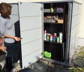 . Eine Frau öffnet einen Gartenschrank mit Reinigungsmitteln und Werkzeugen.