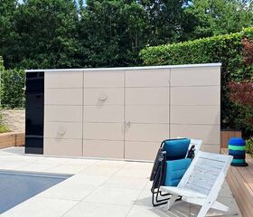 Ein moderner Garten mit einem Pool, hellen Fliesen, einem Geräteschuppen, blauen Stühlen und vielen Bäumen im Hintergrund.