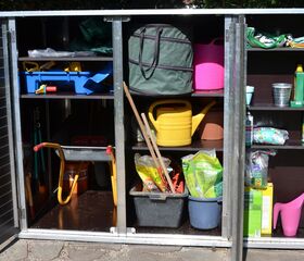 . Ein geöffneter Schrank mit Gartengeräten, Gießkannen, Säcken, Schaufeln und Gartenbedarf.