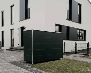 . Modernes Haus mit schwarzem Mülltonnenversteck auf gepflastertem Weg.