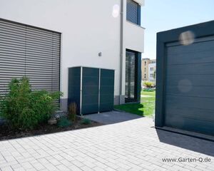 . Ein moderner Gartenbereich mit Schuppen, Pflanzen und Garagentor an einem weißen Gebäude.