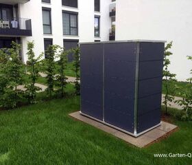 . Ein moderner Gartenschrank steht auf Rasen vor einem Wohnhaus, umgeben von kleinen Bäumen und Gehweg.