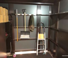 Ein Lagerraum mit Kartons, Reinigungsgeräten, Schaufel, Leiter und Mantel.