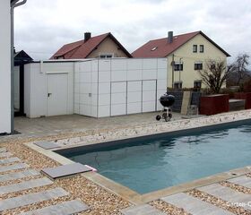 Moderner Garten mit Pool, Steinweg, Grill und Weißem Schuppen, im Hintergrund Häuser.