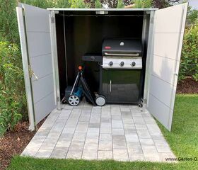 Ein Schrank mit geöffneten Türen zeigt einen Grill und eine Wasserpumpe, umgeben von Gartenpflanzen.