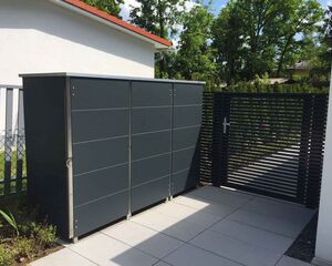 . Ein grauer Außenlagerschrank neben einem modernen Zauntor im Garten.