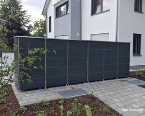 Großer grauer Gartenschrank neben einem modernen Gebäude, umgeben von Pflanzen und gepflastertem Boden.