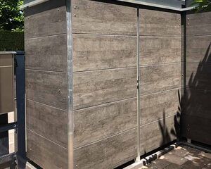 Ein Gartenlager mit Holzdekor NW25 Hesbania, umgeben von Bäumen und Pflastersteinen.