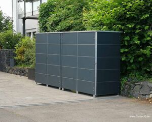Ein moderner, grauer Gartenschrank steht auf einem gepflasterten Hof, umgeben von Pflanzen und Büschen.