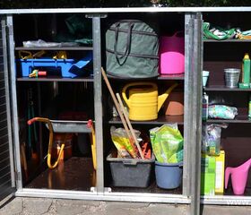 . Ein offener Schrank mit Gartengeräten, Gießkannen, Eimer, Werkzeugkasten und Gartenbedarf.