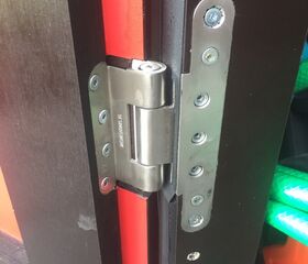 Nahaufnahme eines Türbandes mit sichtbaren Schrauben an einer teilweise offenen schwarzen und roten Tür.