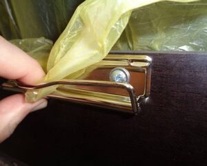 . Eine Hand richtet einen gelben Plastikmüllbeutel in einem Metalleimer mit Schraube aus.