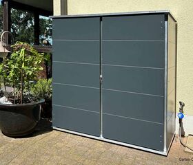 Ein moderner Gartenschrank aus Metall steht neben einem großen Blumentopf auf einer Terrasse.