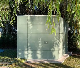 . Ein grünes modernes Gartenhaus unter einem Baum mit herabhängenden Zweigen.