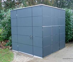 Ein modernes, quadratisches Gartenhaus in einer Hofecke mit grauen Paneelen umgeben von Pflanzen.