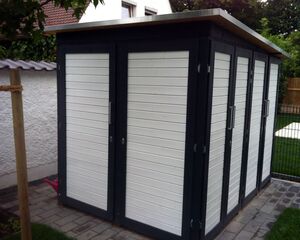 Ein moderner Schuppen mit weißen Paneelen und Metallrahmen auf einer gepflasterten Fläche.