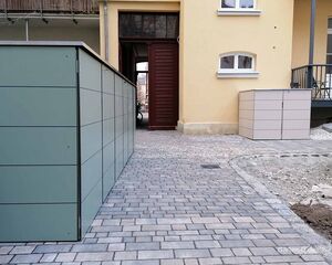 Hinterhof mit gelbem Gebäude, grauen Schränken und gepflastertem Weg.