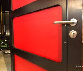 . Rote Tür mit modernem Griff, im Hintergrund ein grünes Fahrrad in einer Garage.